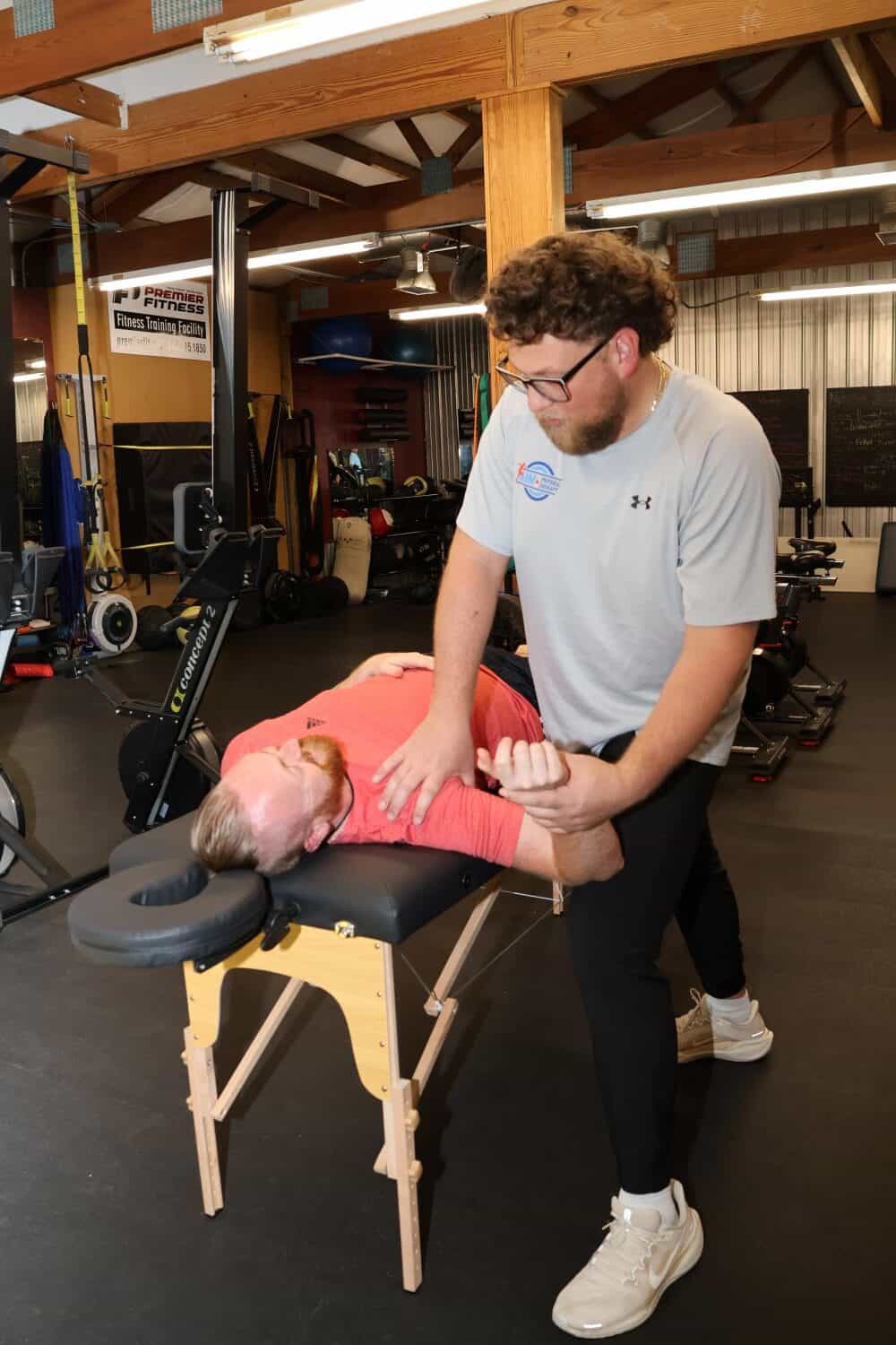 AIMPT - A man performs physical therapy on another man lying face down on a massage table in a gym setting. - Charleston, South Carolina