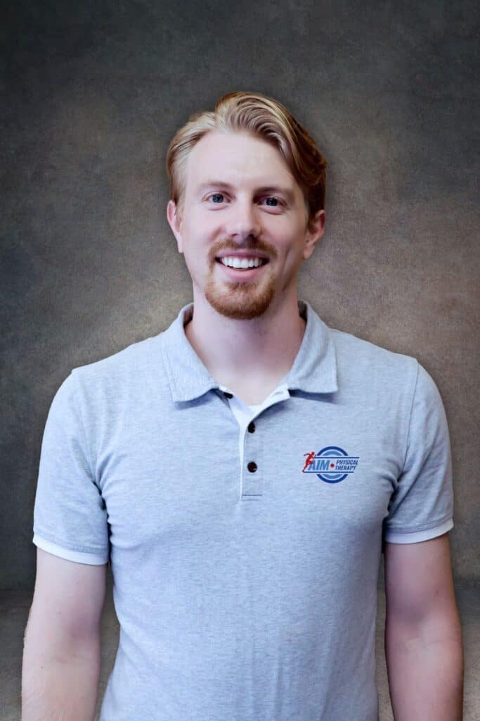 AIMPT - A man with light skin and reddish-blond hair smiles at the camera, wearing a light gray polo shirt with a HIM Motorsports logo, posed against a neutral backdrop. - Charleston, South Carolina