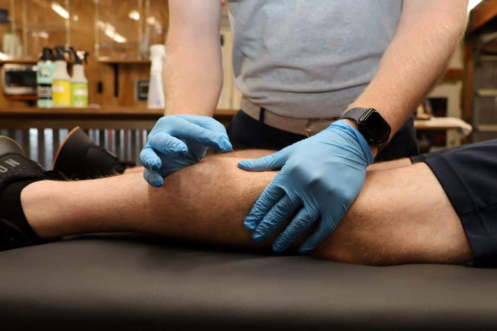 AIMPT - A person wearing blue gloves examines another person's lower leg while they lie on a black examination table. - Charleston, South Carolina