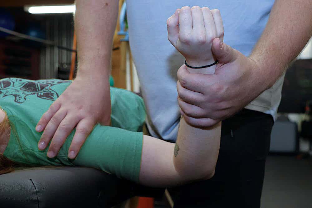 AIMPT - A person lying down receives physical therapy as another person manipulates their bent arm and supports their wrist. - Charleston, South Carolina