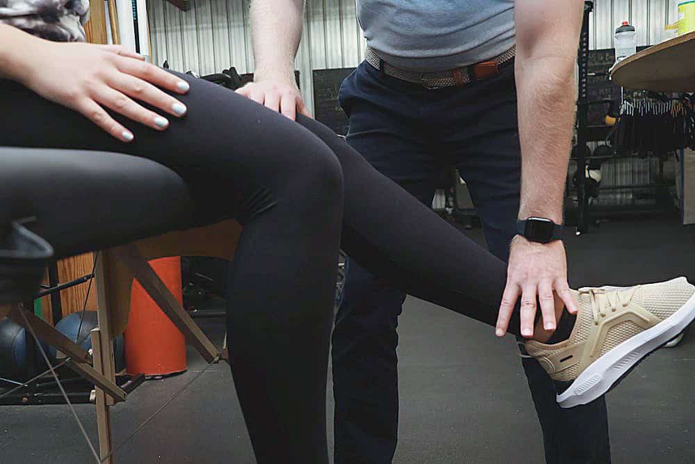 AIMPT - A person sitting with their leg extended while another person, standing, examines or supports their lower leg and ankle. - Charleston, South Carolina